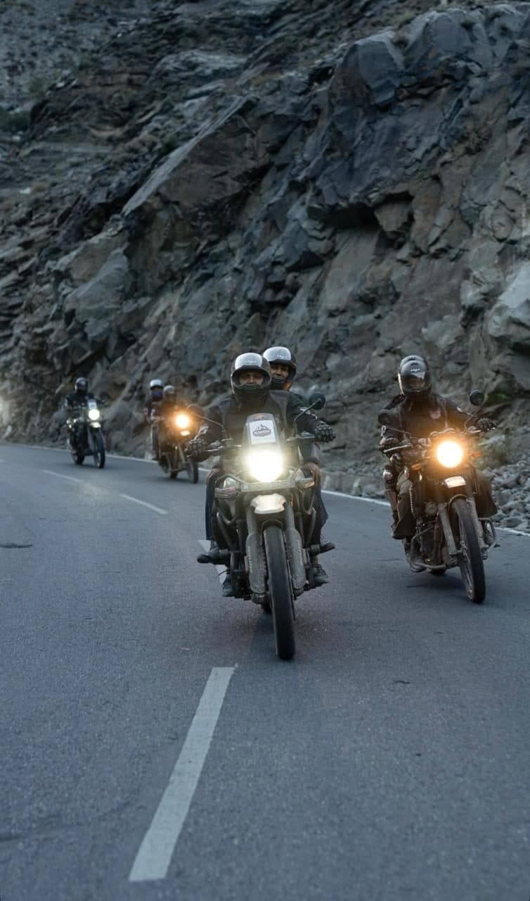 Riders with headlights on, coming down a mountain road at dusk