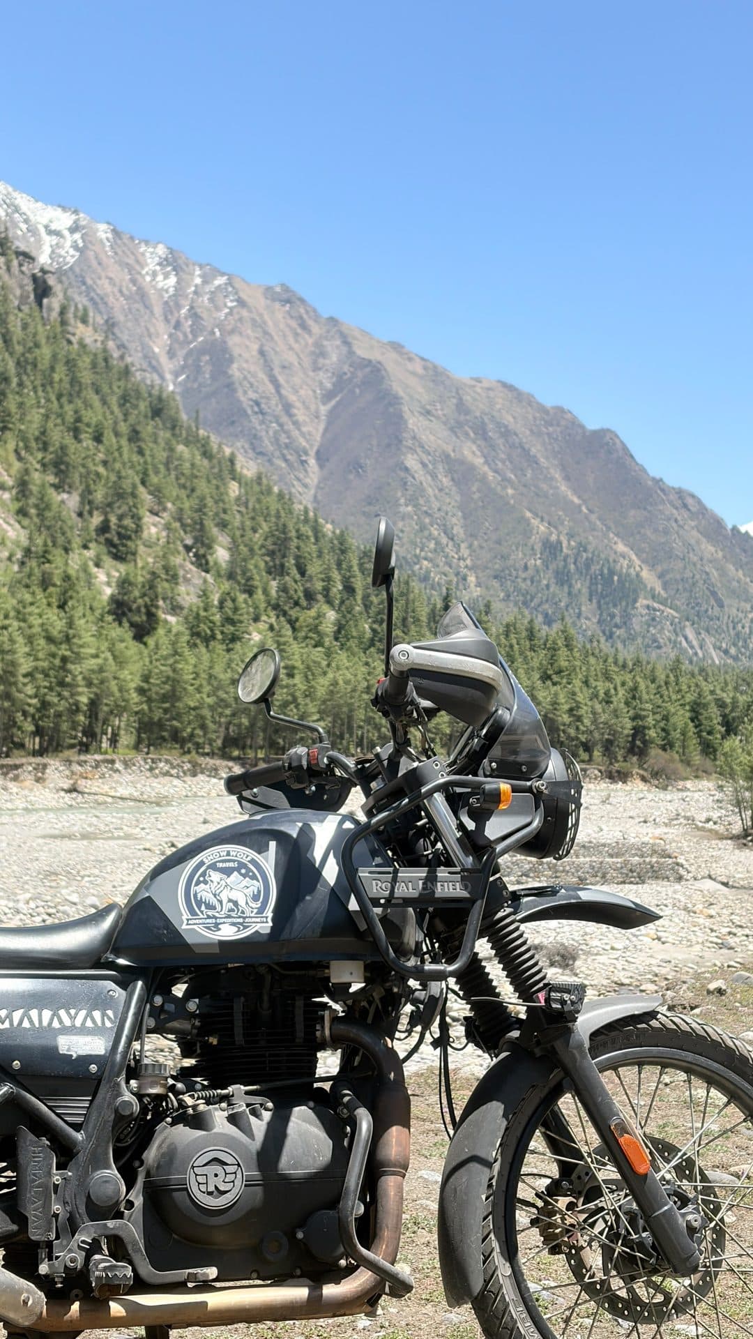 A motorcycle parked on gravel below a steep brown mountain face